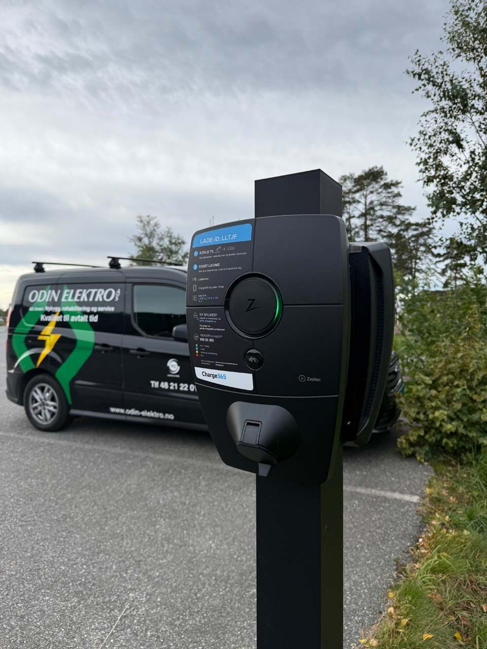 Elbillader på stolpe ved parkeringsplass med servicebil i bakgrunnen